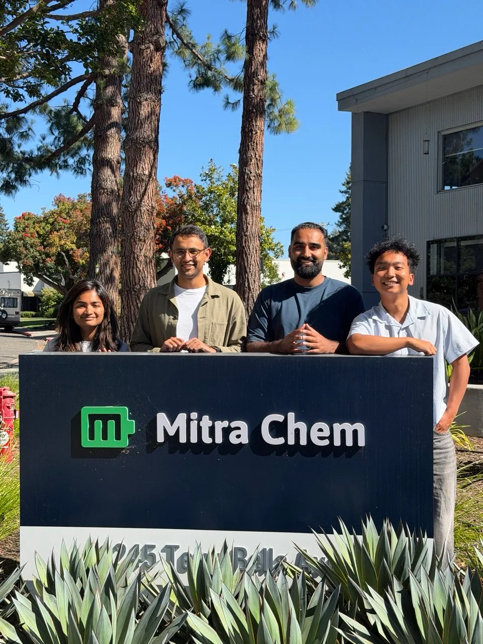 Joshua with colleagues beside the Mitra Chem sign